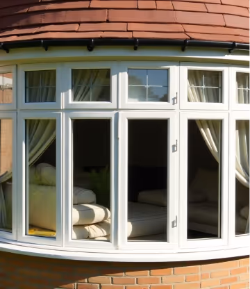White-framed bay windows with closed curtains, offering a glimpse of a sofa in a residential living room.